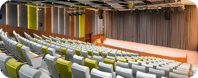 Modern university auditorium designed by an interior design and fit out company, featuring green and grey seating, a wooden stage, and acoustic panels.