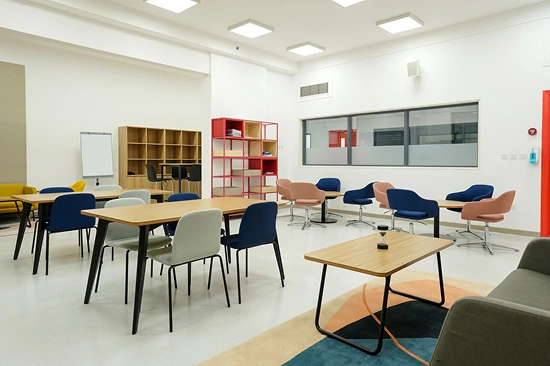 A versatile classroom or breakout area by an interior design and fitout company, with various tables, chairs, shelving, and soft seating for learning spaces.