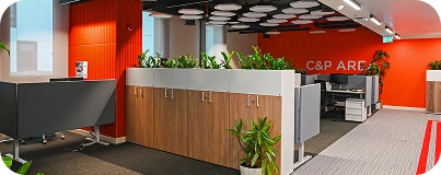 A modern open office and collaboration area by an interior design and fit out company, featuring orange accent walls, tiered wooden seating, and white desks with green plants.
