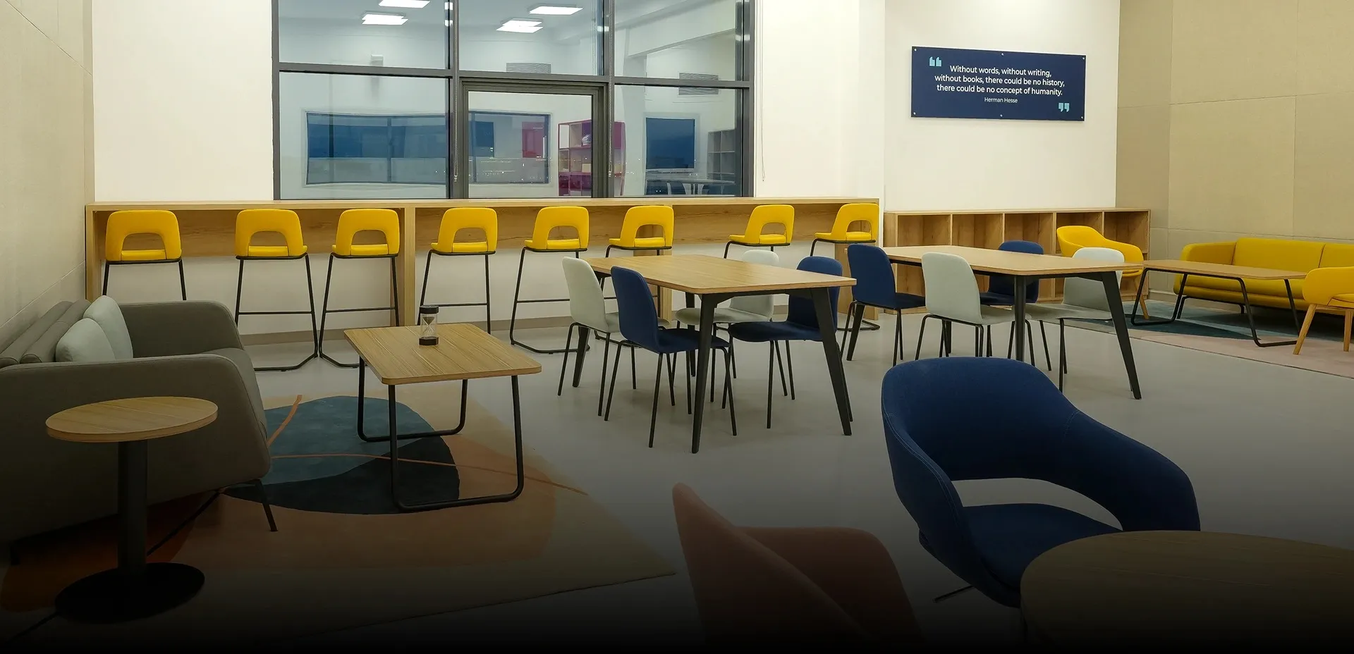 Interior fit-out of a versatile higher education group study area with varied seating, red shelving, and a large window, creating adaptable aesthetics.